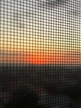 A Captivating Sunset View Through a Mesh Screen, Blending Warm Colors of Tw.. Stock Photos