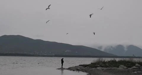 Capture the silhouette of a man against the backdrop of a mountain lake on a Vídeo Stock 252467709