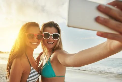 Capturing memories. two friends taking selfies while hanging out at the beach. Stock Photos