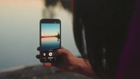 Capturing sunset with mobile device. Serene evening scene at tranquil lakeside Stock Footage 338009253
