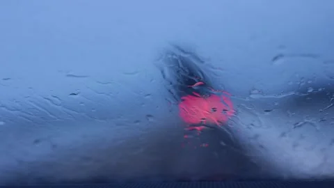 Car ahead in rain seen through wet windshield. Red stoplight bokeh scene. Vídeos de archivo 329625755