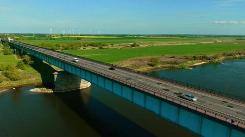 Car and cargo mini bus driving across bridge over river with wind turbines in Stock Footage 323607014