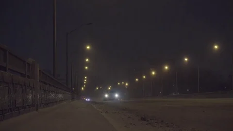 Car approaching on bridge at night during a snow storm Видео 85401799