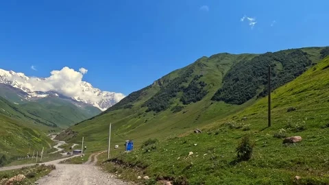 Car approaching Mount Shkhara in wide view along a gravel road from Ushguli Stock Footage 343775176