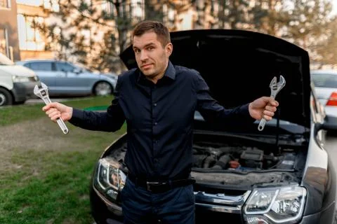 Car breakdown concept. The car will not start. The young man tries to fix Stock Photos