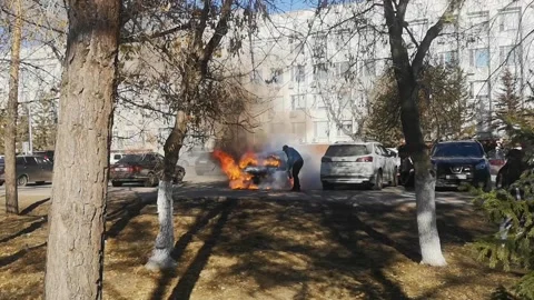 Car burning in parking, strong open flame, fire. man tries to put out fire Stock Footage 287719747