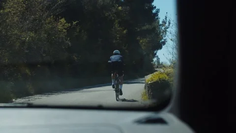Car chasing cyclist riding on a mountain road among high mountains Stock Footage 223521763