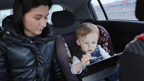 In car. The child is playing on a computer tablet, the mother watches him. Stockbeeldmateriaal 201295928