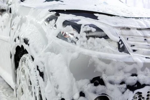 A car covered by soap foam while washing indoors - close-up front wiew with Stock Photos
