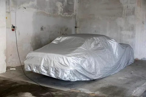 Car covered under silver sheet at garage Stock Photos