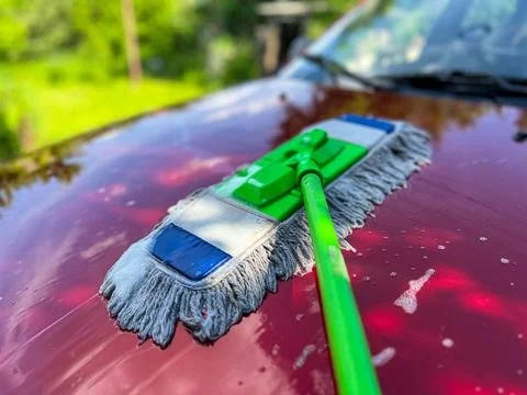 Car detailing using a mop: cleaning red car hood with soapy water Stock Photos