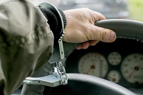 Car driver hand handcuffed to steering wheel, arrest, driving ban Stock Photos