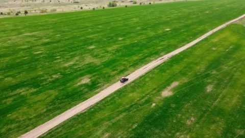 The car drives along the road between green fields, shooting from a drone Stock Footage 233340037