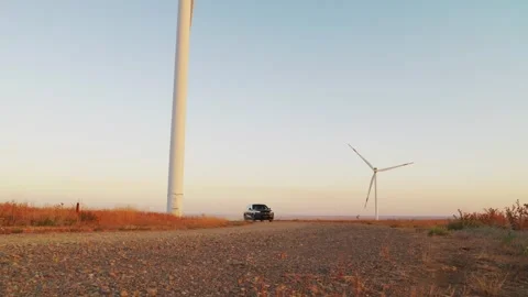 A car drives slowly between wind generators. Glare of the setting sun. Electric  Stock Footage 288193832