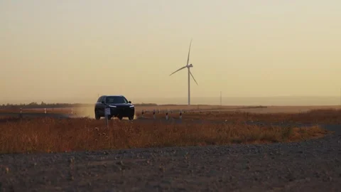 A car drives slowly between wind generators. Glare of the setting sun. Electric  Stock Footage 288194011