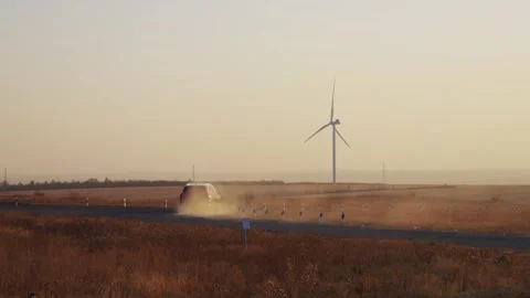 A car drives slowly between wind generators. Glare of the setting sun. Electric  Stock Footage 288194019