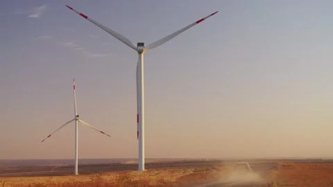 A car drives slowly between wind generators. Glare of the setting sun. Electric  Stock Footage 288194026