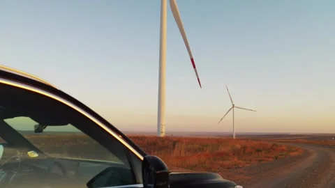 A car drives slowly between wind generators. Glare of the setting sun. Electric  Stock Footage 288194035