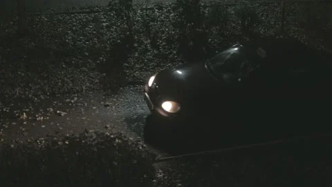 The car drives into the yard at night with the headlights on in cloudy weather i Stock Footage 163687854