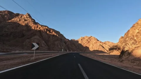 Car driving on desert highway between rocky mountains under clear blue sky at Stock Footage 326025223