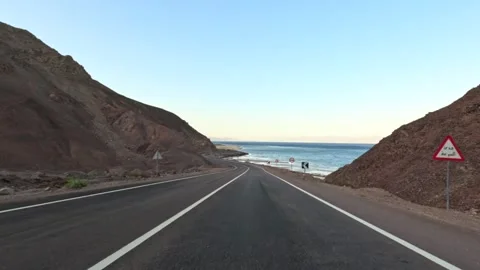 Car driving on desert highway between rocky mountains near sea at sunset Stock Footage 340868834