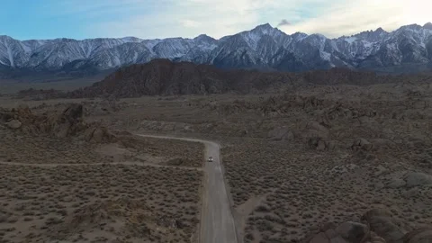 Car Driving down Dirt road in front of Snow Capped Sierra Nevadas at Dusk Stock Footage 305279489