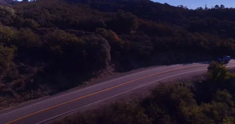Car driving down empty winding road in the mountains Stock Footage 136341376