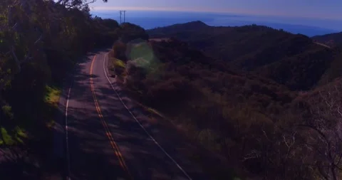 Car driving down empty winding road in the mountains Stock Footage 136341425