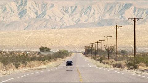 Car driving down hot desert road with mountain background Vídeo Stock 99211457
