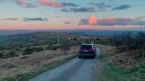 Car driving down a lane in the evening light from Kit Hill over the Tamar Valley Stock Footage 262626144