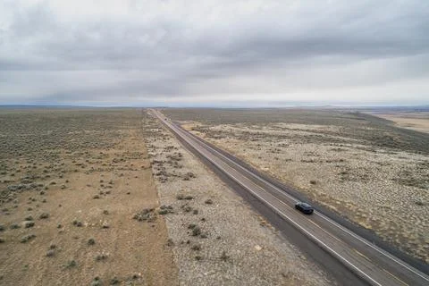 A car is driving down a long, empty road in a desert Stock Photos