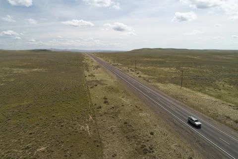 A car is driving down a long, empty road in a desert Stock Photos
