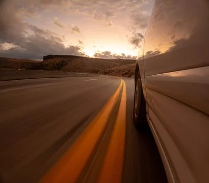 A car is driving down a road with a sunset in the background Stock Photos