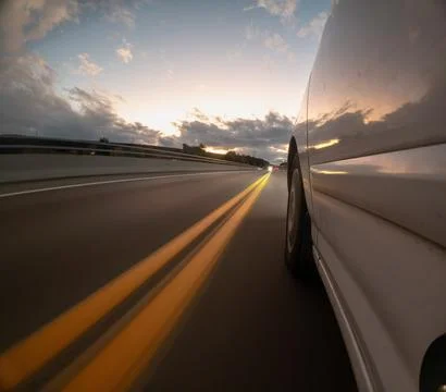 A car is driving down a road with a sunset in the background Stock Photos