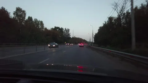Car Driving At Dusk Down Tree-Lined Road With Headlights On Seen Through Windshi Vídeos de archivo 335448454