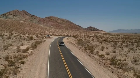 Car driving empty desert road with mountain background - drone flying forward Stock Footage 107879563