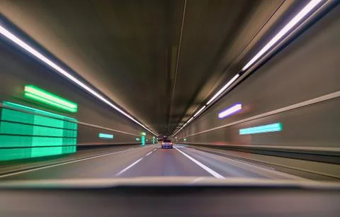 Car driving fast down interior tunnel, following another car. Stock Photos