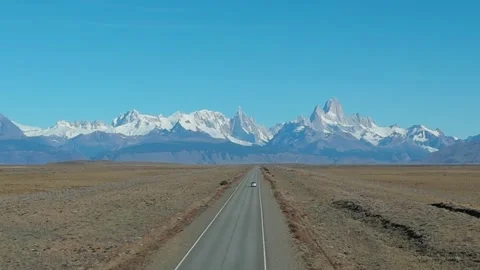 Car driving on a long straight road towards snow capped mountain peaks . Stock Footage 341993638