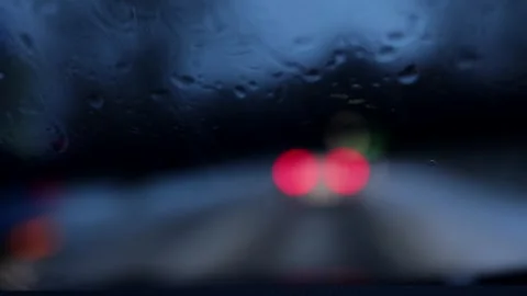 Car driving in rain seen through wet windshield. Night traffic bokeh scene. Stock Footage 329625764
