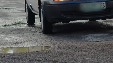 Car driving through pothole in the road filled with water after rain Stock Footage 229334165