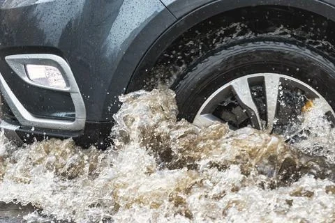 The car is driving through a puddle in heavy rain. Splashes of water from und Photos