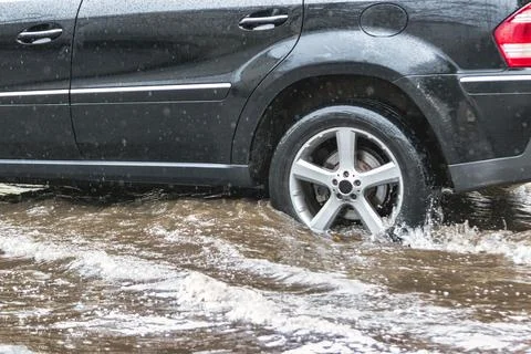 The car is driving through a puddle in heavy rain. Splashes of water from und Photos