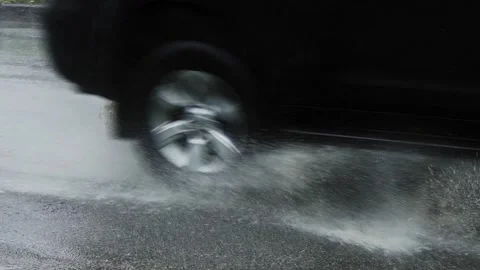 Car driving through puddles creating splashes of rainwater around. slow motion. Stock Footage 258984937