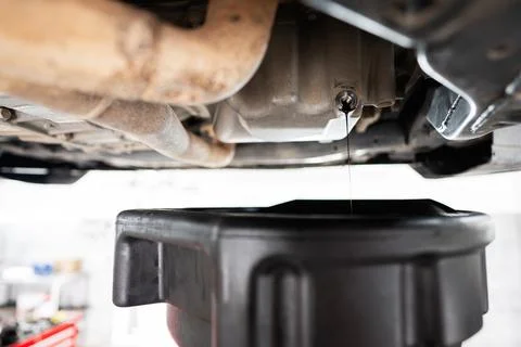 Car engine oil change process with oil draining pan below Foto stock