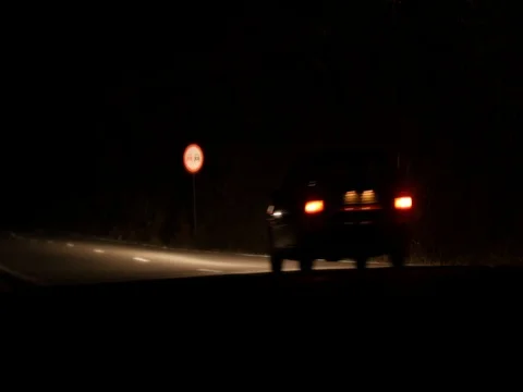 Car that goes by speed on a paved road all night illuminating the road with i Vídeos de archivo 80262751