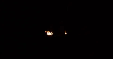 Car headlights ominously drive through a dark thick forest brush at night Stock Footage 122076477