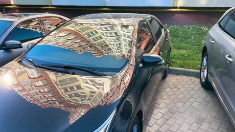 Car hood and windshield reflect modern residential buildings.  Stock Footage 338240260