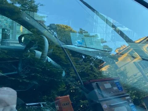 Car interior showing reflections on windshield of street, buildings, and tr.. Stock Photos