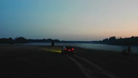 A car with its headlights on after sunset passes through a field filled with fog Stock Footage 161810569