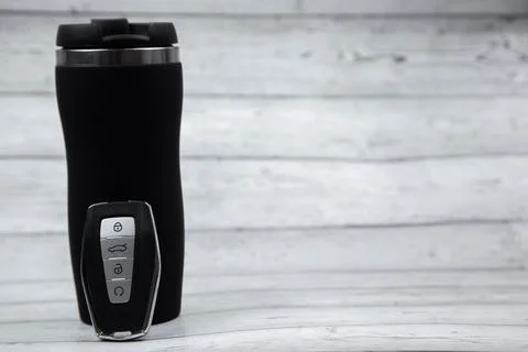 The car key is black with metal automatic buttons, leaning on a black thermocup Stock Photos